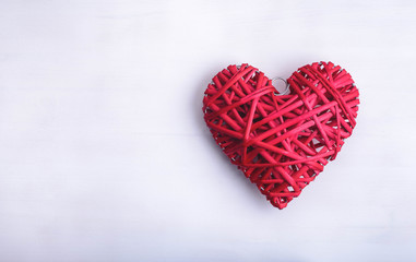 Red decorative handmade wicker heart on the white wood background. 