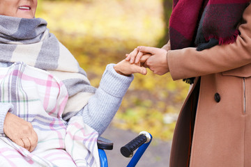 Disabled senior woman and young caregiver in park, closeup