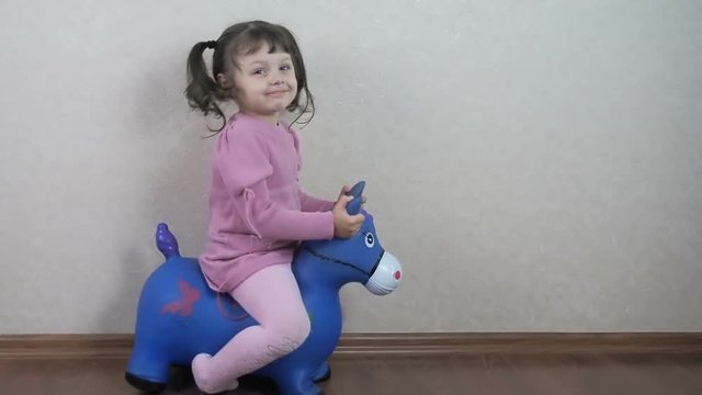 The child is playing with a toy donkey. Beautiful little girl is sitting on a toy donkey.