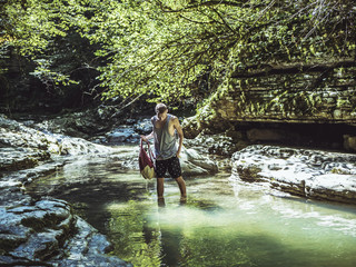 man walking in the mountain canyon river stream with backpack