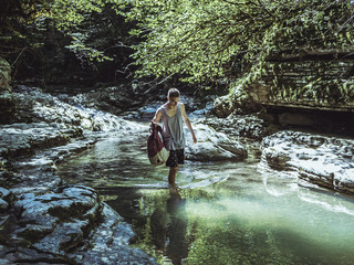 man walking in the mountain canyon river stream with backpack