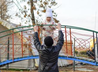 Dad plays with his daughter on the playground in the park. Autumn walk of the family.