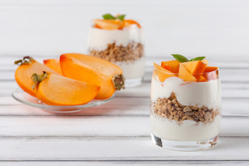 Persimmon creamy trifle in beautiful glasses, fresh ripe fruit slices on white wooden background. Healthy vegetarian food. Delicious dessert. Close up photography. Selective focus.