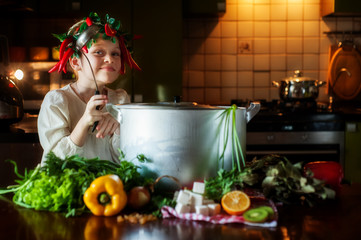 A girl with red peppers on her head is standing next to the table with a ladle.