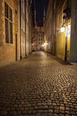 Fototapeta na wymiar View of cobblestone paving on the empty Kramarska Street and St. Mary's Church at the Main Town (Old Town) in Gdansk, Poland, in the evening.