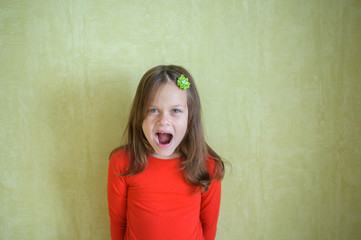 A little girl with a hairpin in her hair and a red sweater stands by the green wall and screams © Kiryakova Anna