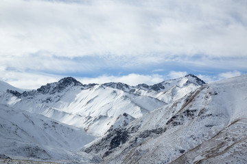 Fototapeta na wymiar Зимний пейзаж. Красивые горы в снегу, белые облака на синем небе над живописным ущельем. Припрда Северного Кавказа
