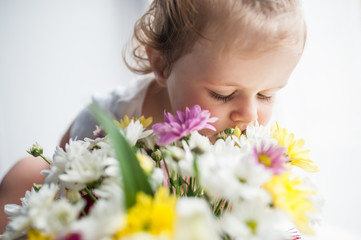 Fototapeta premium Baby sitting and sniffing a bouquet of flowers from small chrysanthemums, closing his eyes and sticking his nose in the flowers