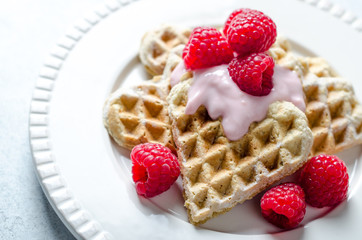 Homemade heart-shaped waffles with raspberries and  redcurrant on a white plate
