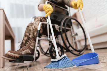 A female veteran in a wheelchair is cleaning the house. She's in military uniform.