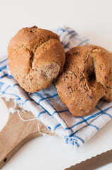 Loaf of rustic farmers market wholegrain rye bread with fried onion baked in a woode fired oven on kitchen towel and wooden cutting board with bread knife on white background