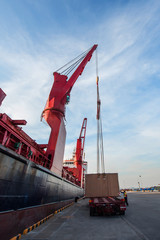 Heavy lift crane being operating by takes loading the cargo shipment from the lowbase trailer in port terminal, where the sea and land transports meet together for logistics worldwide services