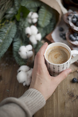 a cup of coffee in a woman's hand, a wooden background and muffins with blueberries