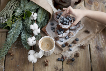 Fototapeta na wymiar a cup of coffee in a child's hand, a wooden background and muffins with blueberries