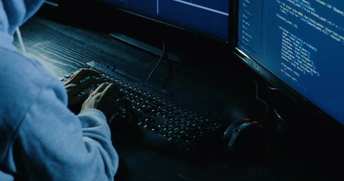 acker in hood cracking code using laptop and computers from his dark hacker room