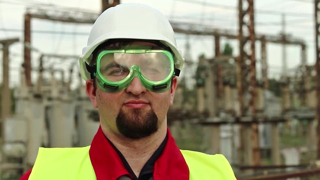Worker in green goggles on electric station looks at the camera. Power engineering specialist in goggles and hard hat at heat power plant