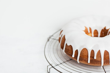 Homemade lemon bundt cake with thick lemon icing on cooling rack on white wooden table