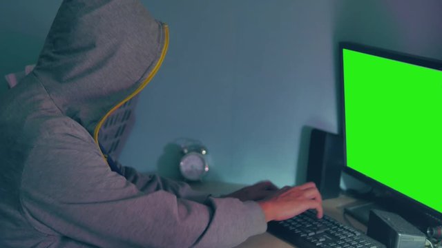 Male hacker internet working on a computer. man hacker in hood hiding his face indoor