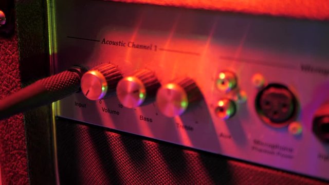 Plugging in cable into the headphone jack of amplifier. Male hand connecting and disconnecting guitar cord to amp. Red neon light. Preparing for music concert.