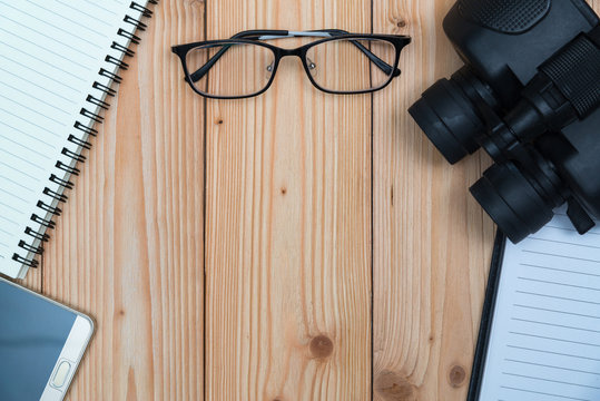 Essential vacation items, sneakers, glasses, smart phone, binocular, notebook and pen on wooden floor, top view with copy space, Travel and vacation concept.