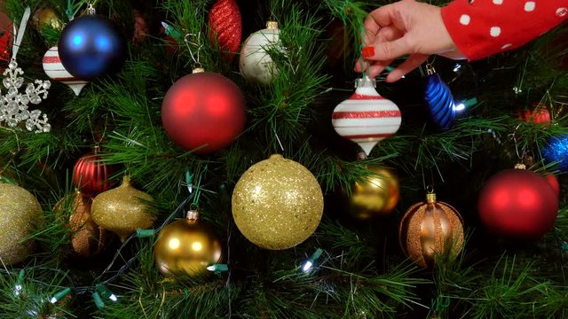 Festive Christmas Tree with brightl color decorations, woman hanging last ornament.