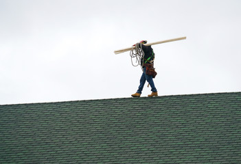 Manual roof repair worker walking on the roof carrying lumber wood - Powered by Adobe