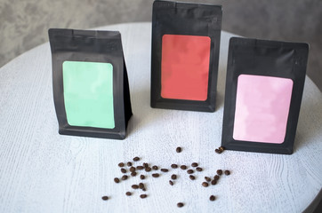 Black coffee packing with sticker stands on white table. Spilled coffee beans