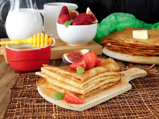 A pile of crepes decorated with a strawberry and a fig. Breakfast on a wooden background
