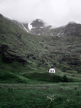 Kleines Haus steht in gr&uuml;ner idylle vor gro&szlig;em Berg der in den Wolken verschwindet