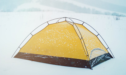 a yellow tent covered with snow on a cold winter day. Winter tent camp in the snow forest © Dima