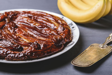 Traditional homemade banana caramel pie on dark grey background. French tarte tatin. Upside down banana cake. Selective focus. Toned image 