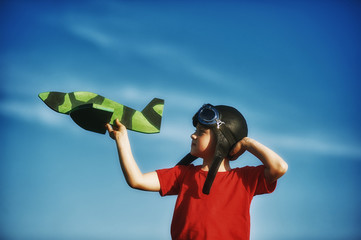 a boy playing with a wooden model of the plane . The child is dressed in leather helmet and goggles . Childhood dreams of becoming a pilot