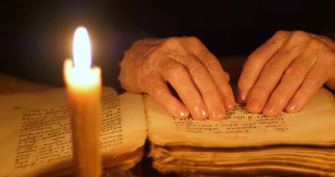 Elderly woman reading old book by candlelight

