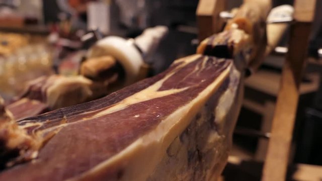 Jamon serrano.Traditional Spanish ham in the market close up.Pork leg ham on table. Gourmet Meat in restaurant interior.Whole jamon on stand.camera moving from right to left