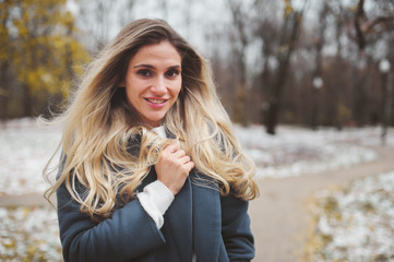 winter portrait of young woman walking in snowy city park in warm grey coat