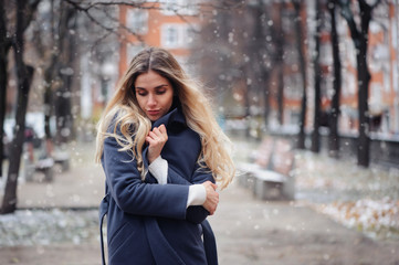 winter portrait of young woman walking on city streets in snowy day, wearing warm grey coat