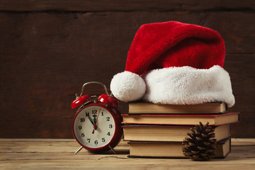 Red alarm clock, fir cone. On the books Santa's hat, on a wooden background