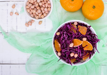 Dietary spicy salad of red cabbage, tangerine and raw peanuts in a ceramic bowl on a white wooden background. Top view. Lenten vegetarian dish.