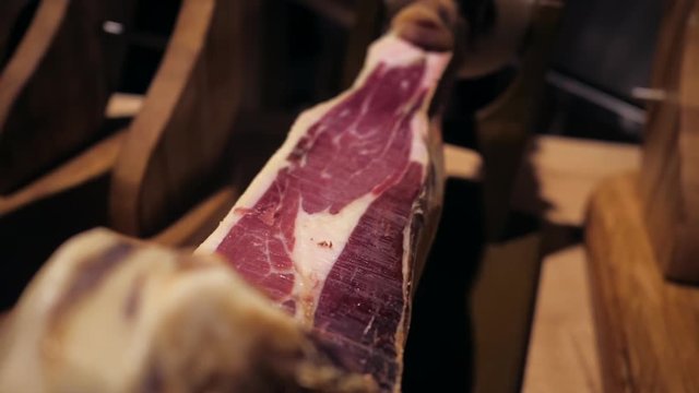 Jamon serrano.Traditional Spanish ham in the market close up.Pork leg ham on table. Gourmet Meat in restaurant interior.Whole jamon on stand.camera moving from right to left