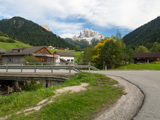 Obraz premium Asphalt road from low point in Alps mountains at hills and mountain village background. Road trip concept, Italy, autumn 2017