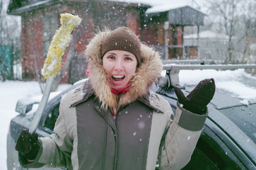 Woman in stress from cleaning the car from snow. Car in snowfall.