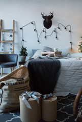 Bed with knitted blanket and pillows with decor indoors. Interior of bedroom with white wall.