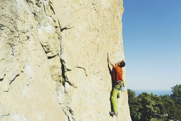 A man rock climbing on rocks against the background of the sea.