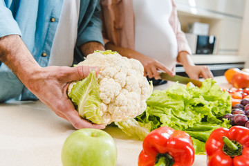 man and pregnant woman at kitchen with vegetables