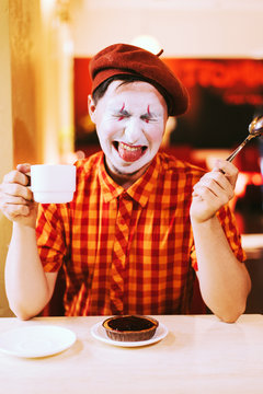 The clown is eating a cake in a cafe and his face is croaking.