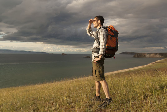 young tourist man with a backpack on the lake, Lake Baikal, summer tourist walk, freedom and happiness