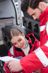 attractive male and female paramedics reading documents in front of ambulance