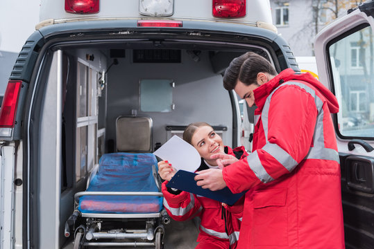 happy male and female paramedics reading documents in front of ambulance