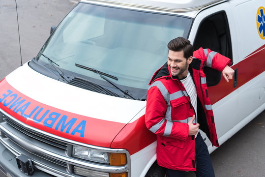 smiling handsome male doctor standing and leaning on ambulance