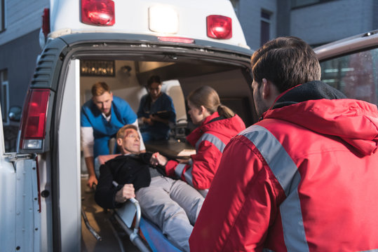 team of paramedics moving wounded mature man into ambulance